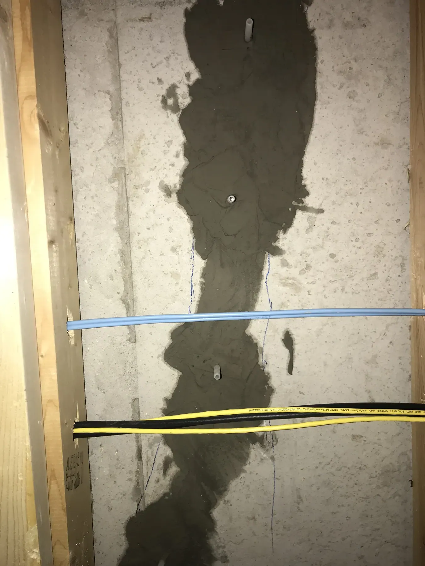 Sealed crack with injection ports in a poured concrete basement wall, exposed between wood studs with network and coaxial cables running across it