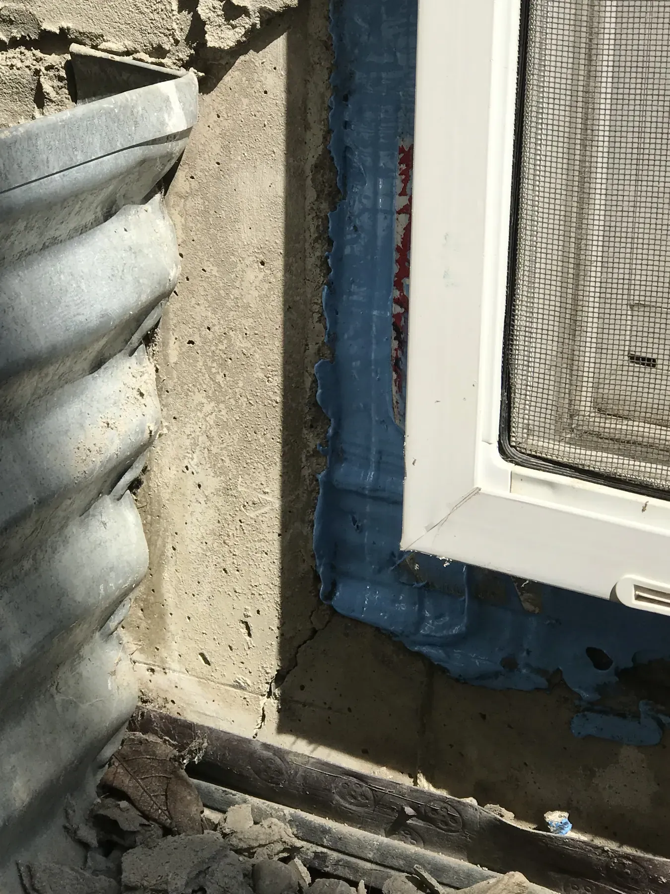 Blue self-adhered membrane flashing around a new basement window frame next to a steel window well
