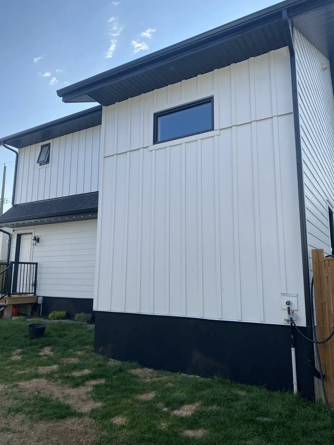 White board and batten siding over a black parged foundation