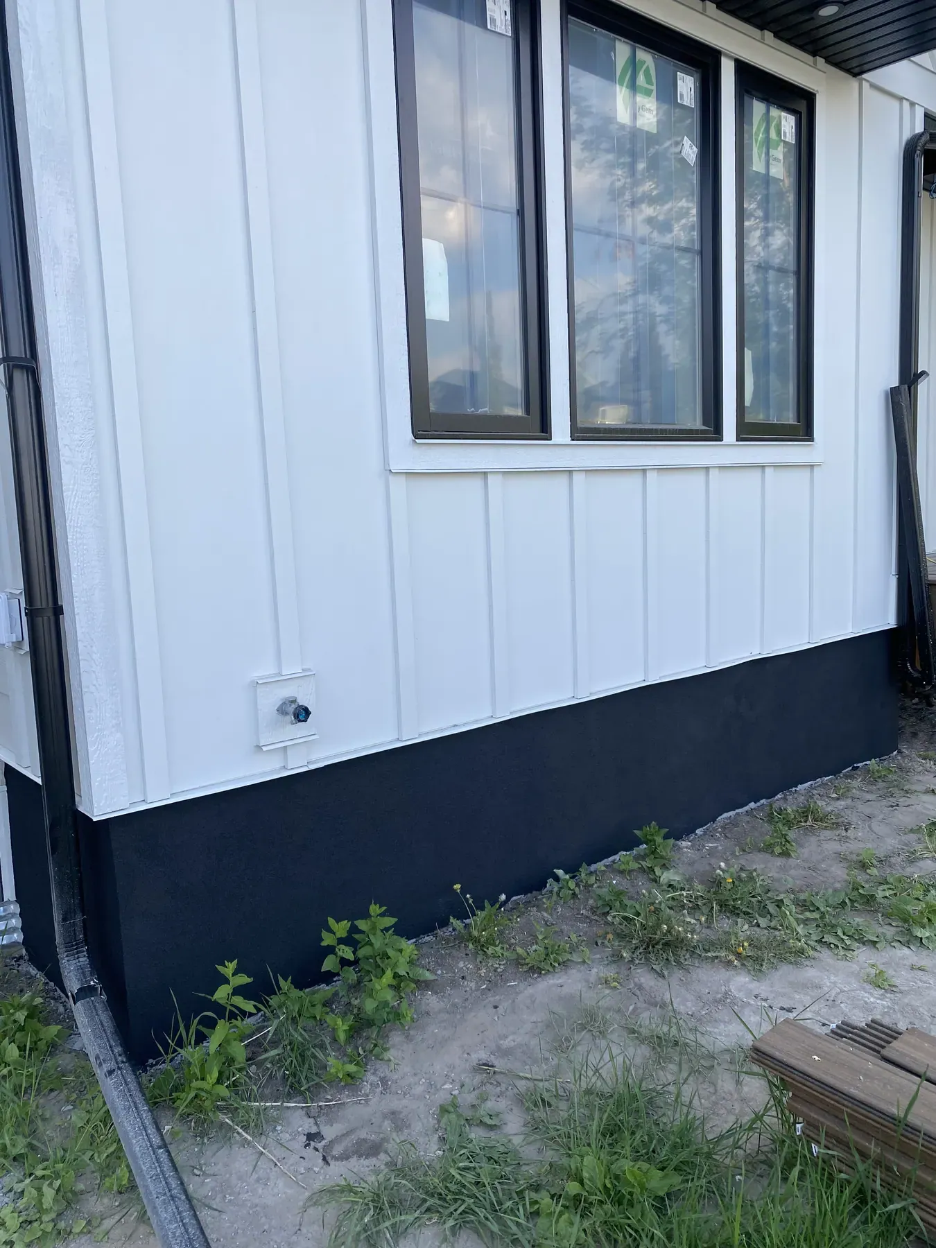 White board and batten siding around new black-framed windows above a black parged foundation
