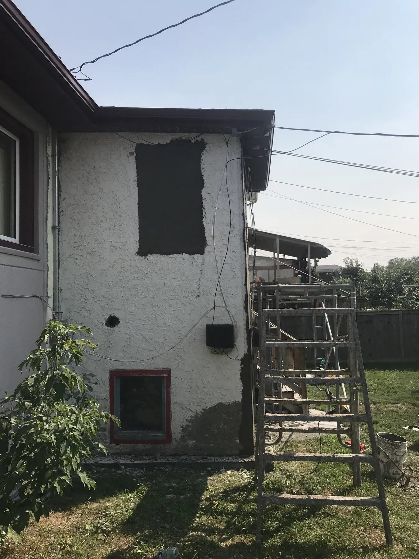 Side wall of a bungalow with old white stucco, a dark patched section and a hole before repair
