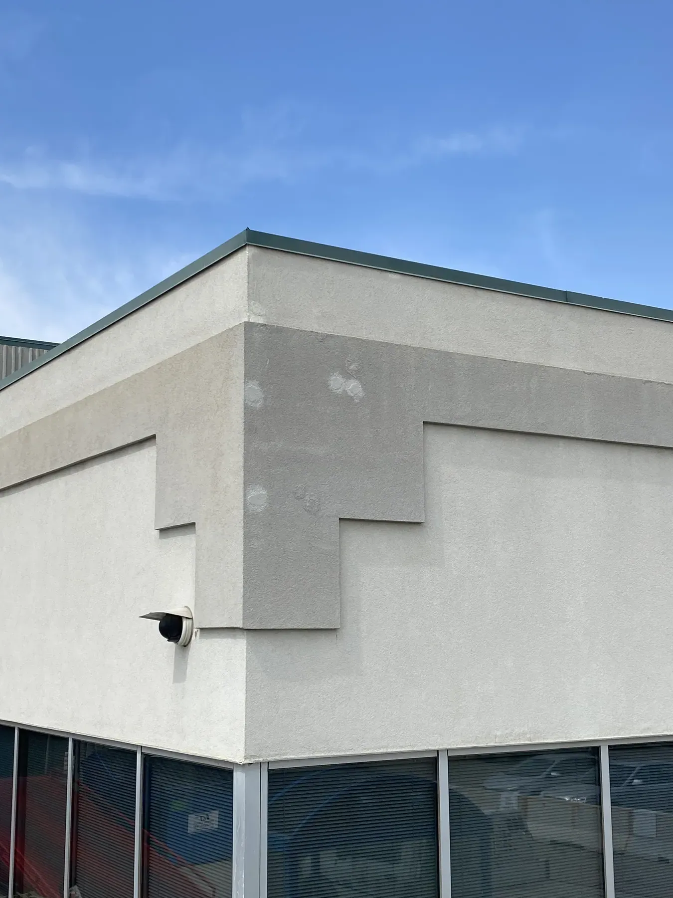 Light grey EIFS cornice on a commercial plaza corner with visible patched spots above the storefront windows