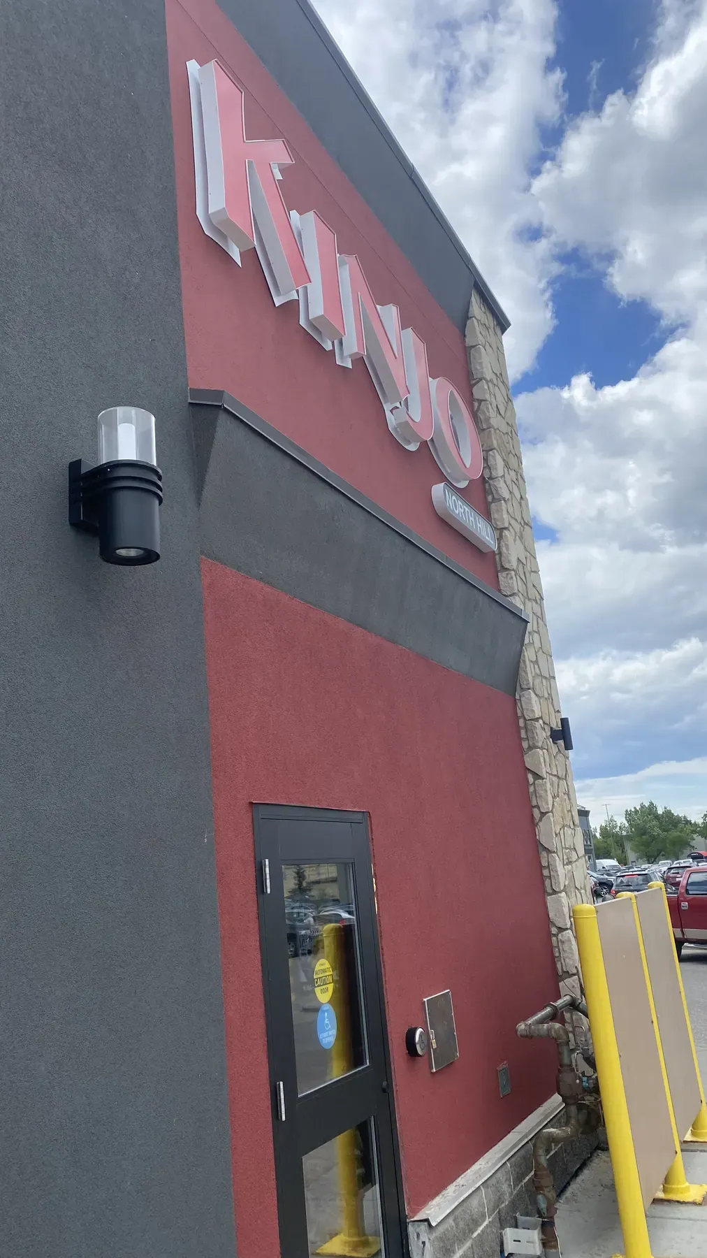 Side elevation of a restaurant with red and charcoal stucco, a stone pilaster and a steel service door