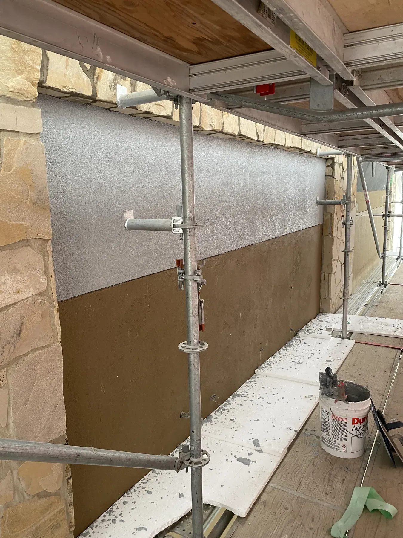 Commercial wall under scaffolding and hoarding with fresh stucco base coat below a finished textured band