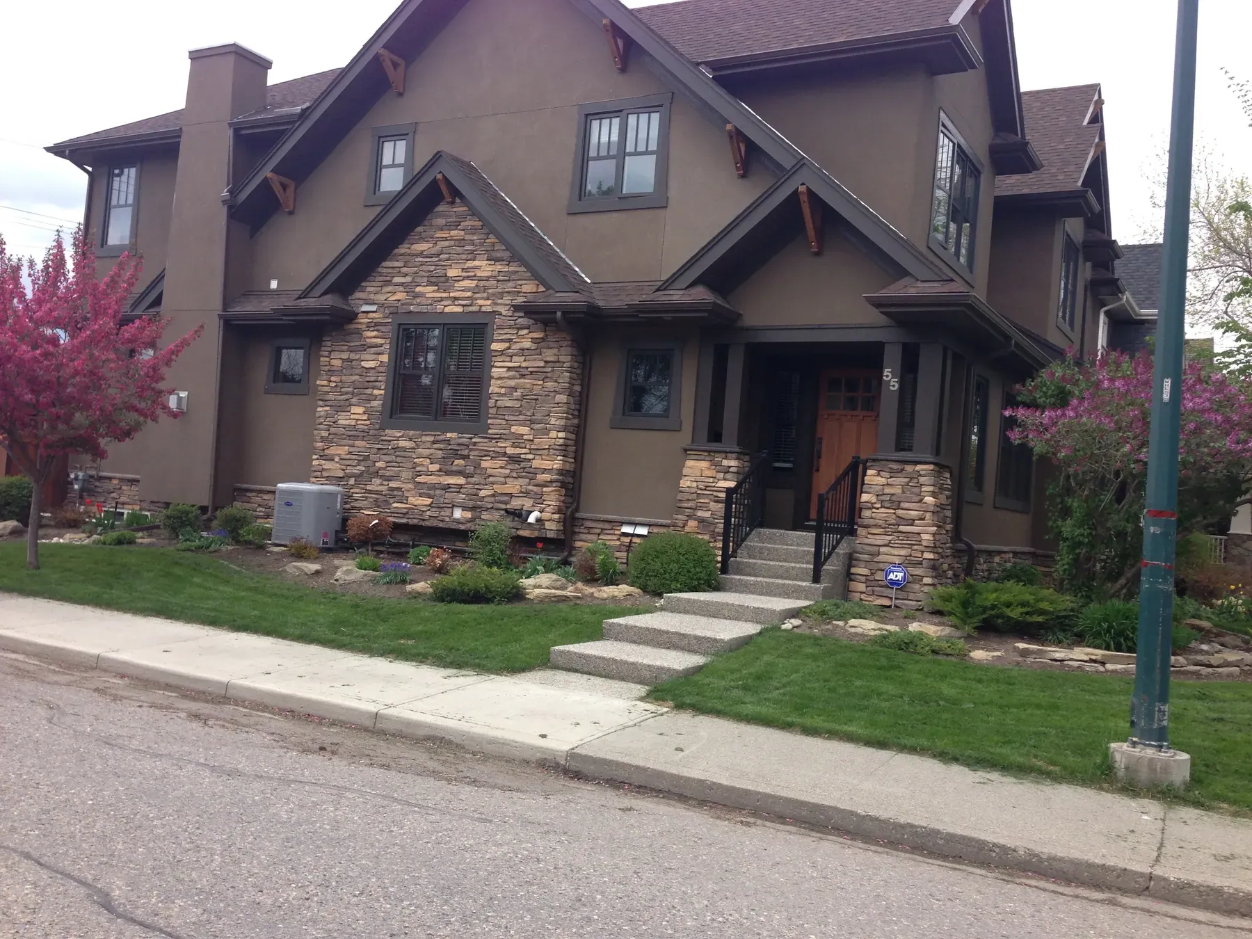 Craftsman style duplex with brown siding, cultured stone columns and gabled rooflines on a corner lot