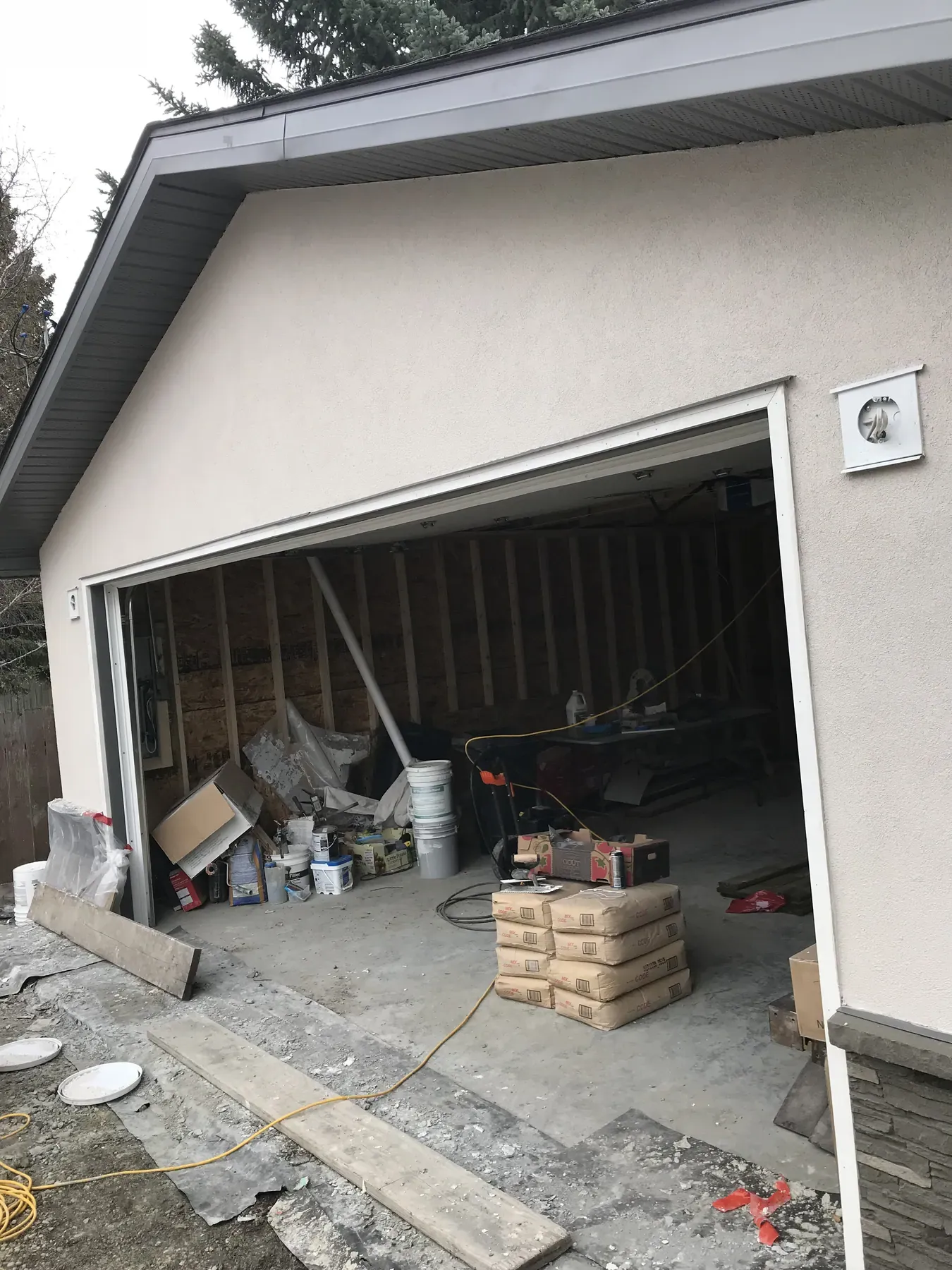 Detached garage under construction with finished stucco outside and open framing, cement bags and materials inside