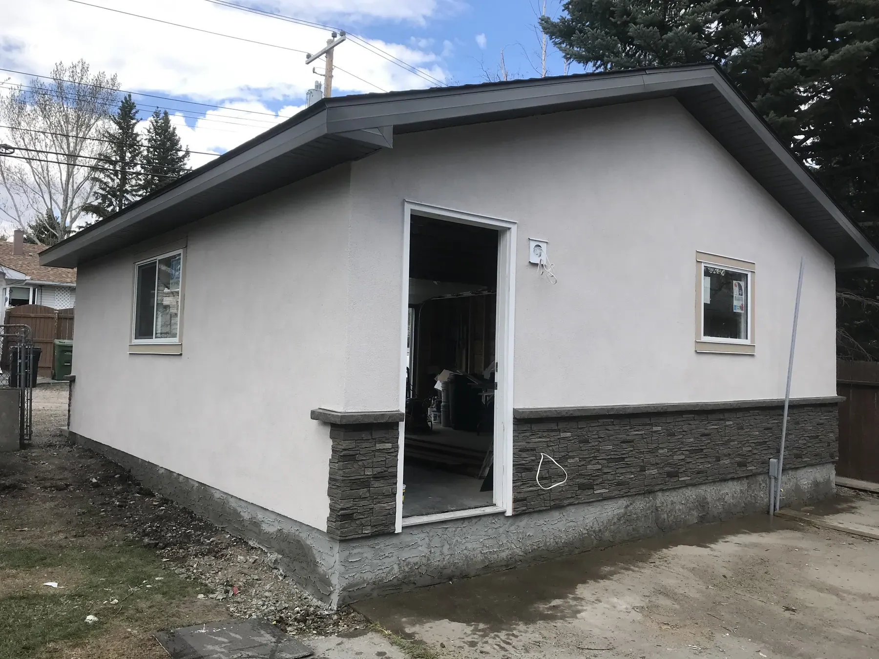 Detached garage with grey stucco walls, stone skirting and a white overhead door