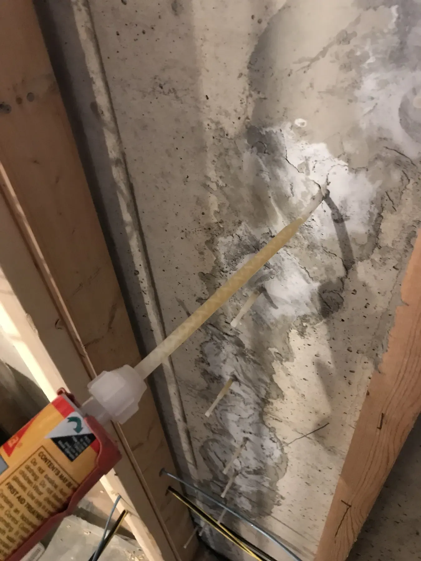 Injection ports and a cartridge gun sealing a crack in a poured concrete basement wall, between wood wall framing