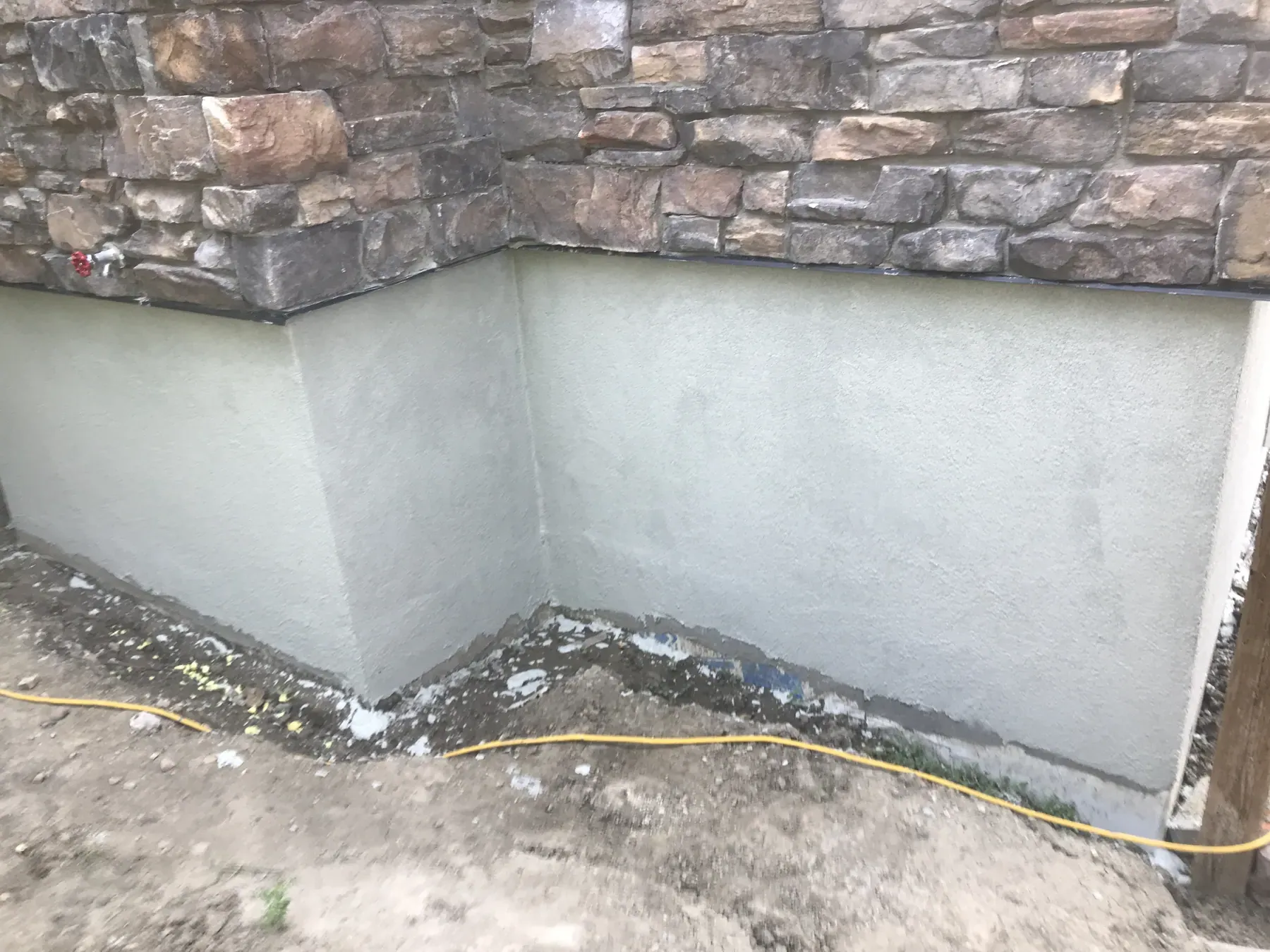 Light grey parging on a foundation wall below brown stacked stone veneer, before backfill