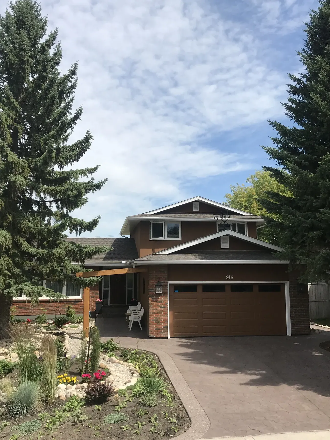 Two-storey Calgary home with brick and brown siding, a stamped concrete driveway, a timber pergola and new landscaping