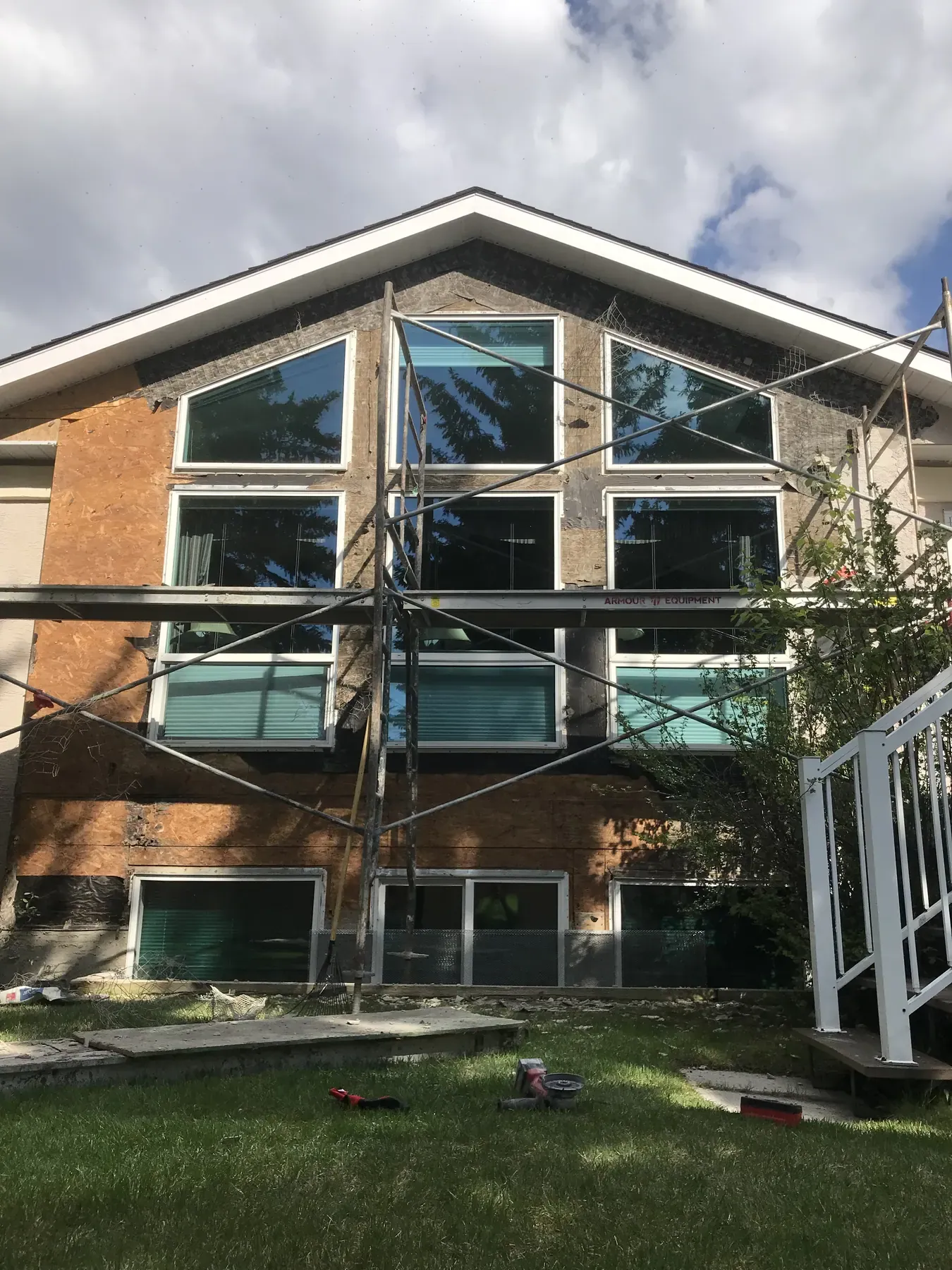 Tall gable wall of windows with the old stucco stripped back to the sheathing behind scaffolding