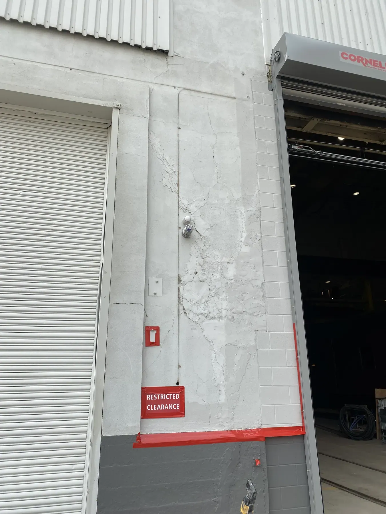 Cracked and broken wall finish between two overhead doors on an industrial building, before repair