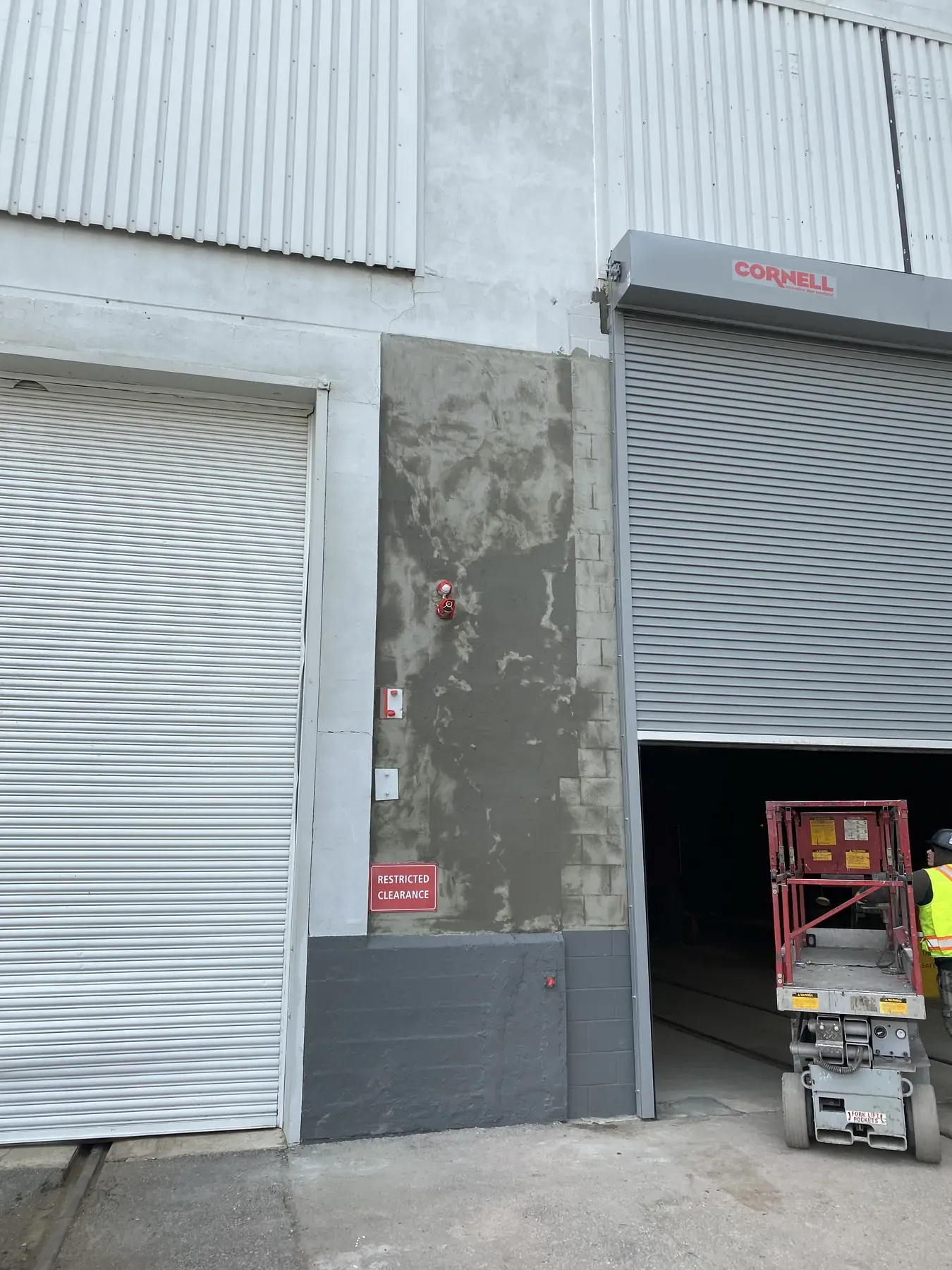 The same industrial wall after a new base coat patch, with a scissor lift at the open overhead door