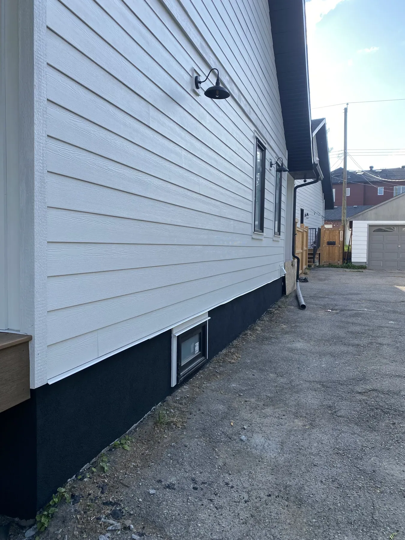 White lap siding with a wood-grain texture over a black parged foundation along a back lane