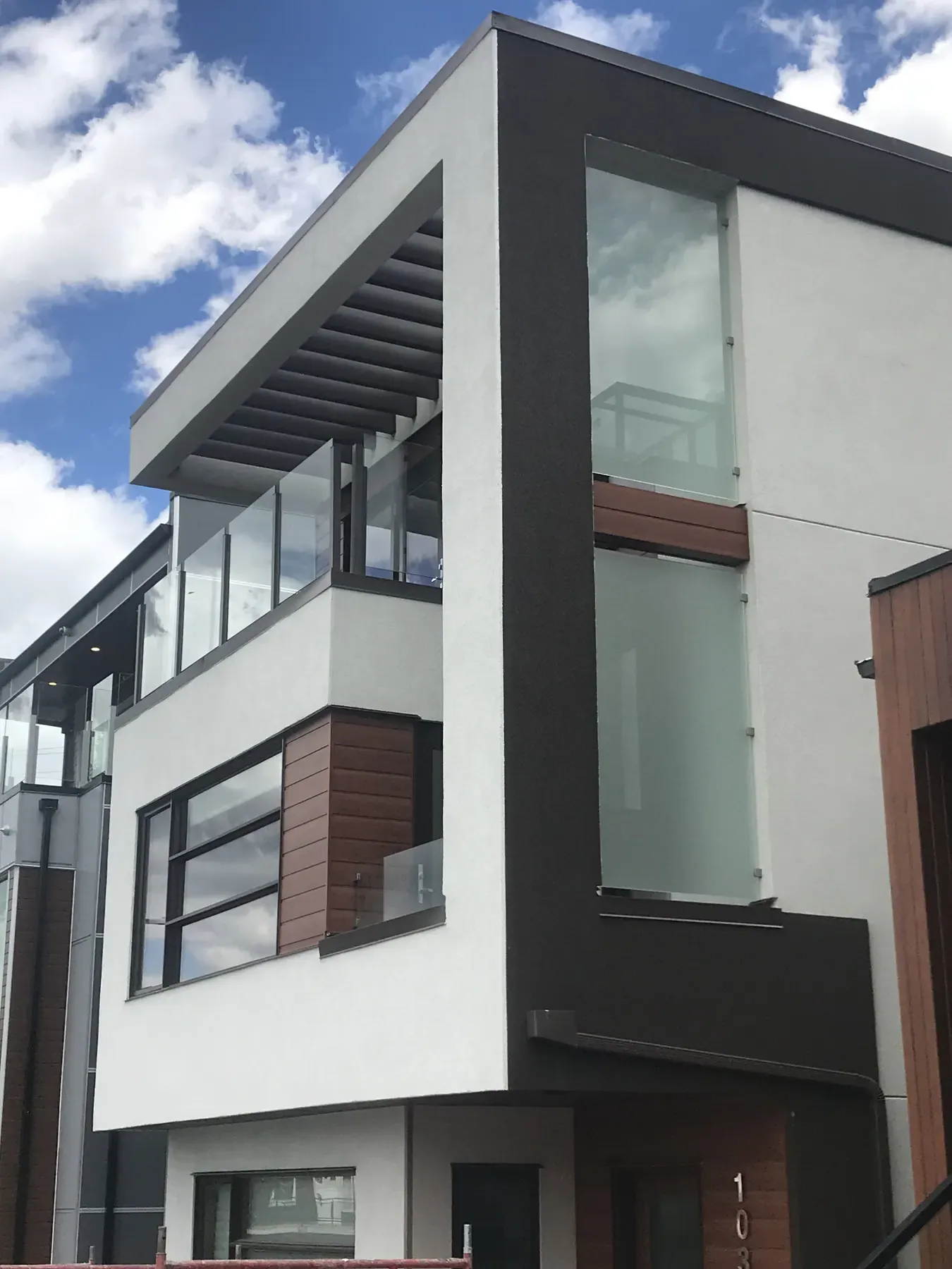 Three-storey modern infill with white and charcoal smooth wall finishes, wood accents and glass balcony railings