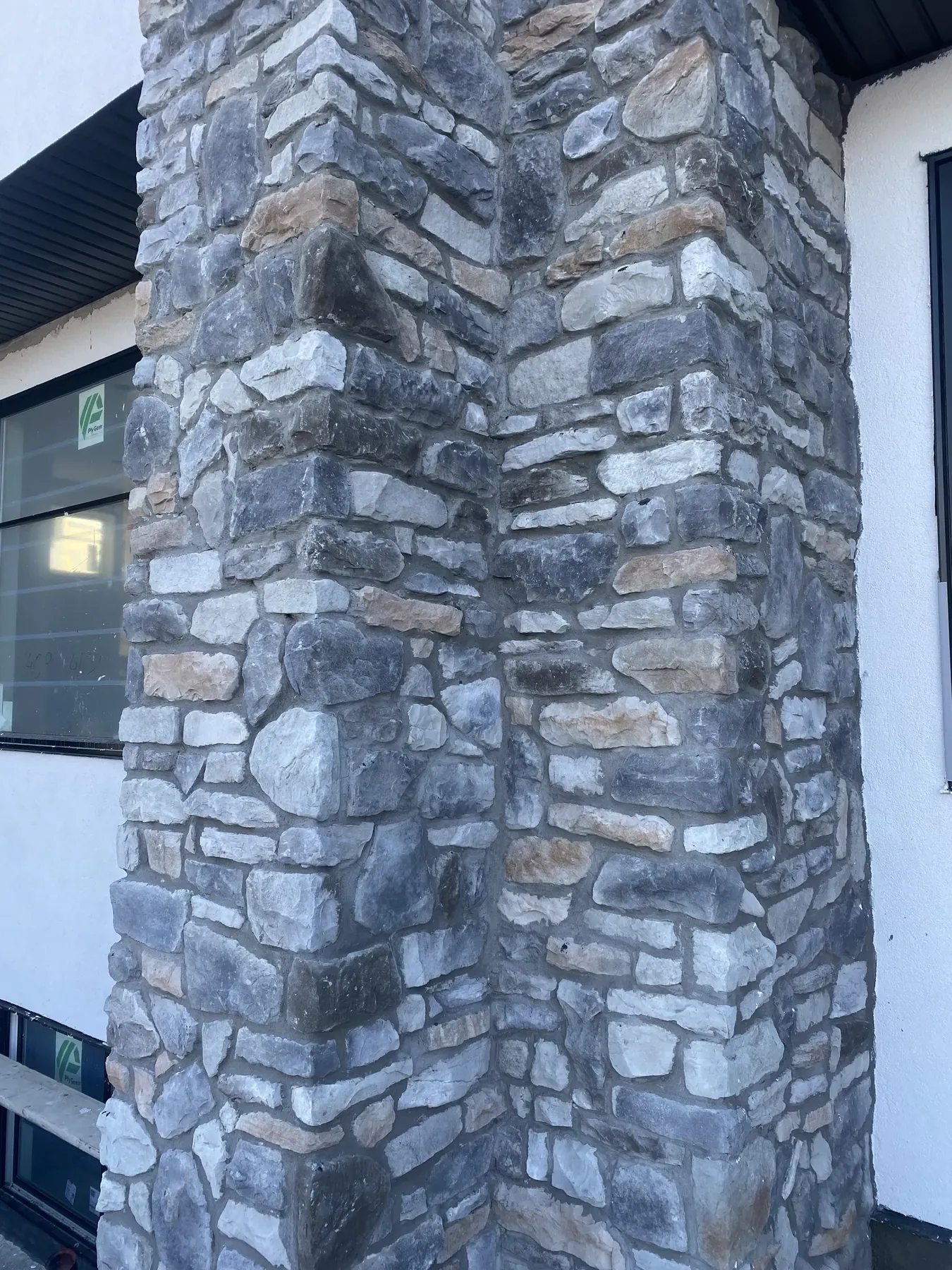 Corner column clad in grey and tan natural stone veneer beside white stucco walls