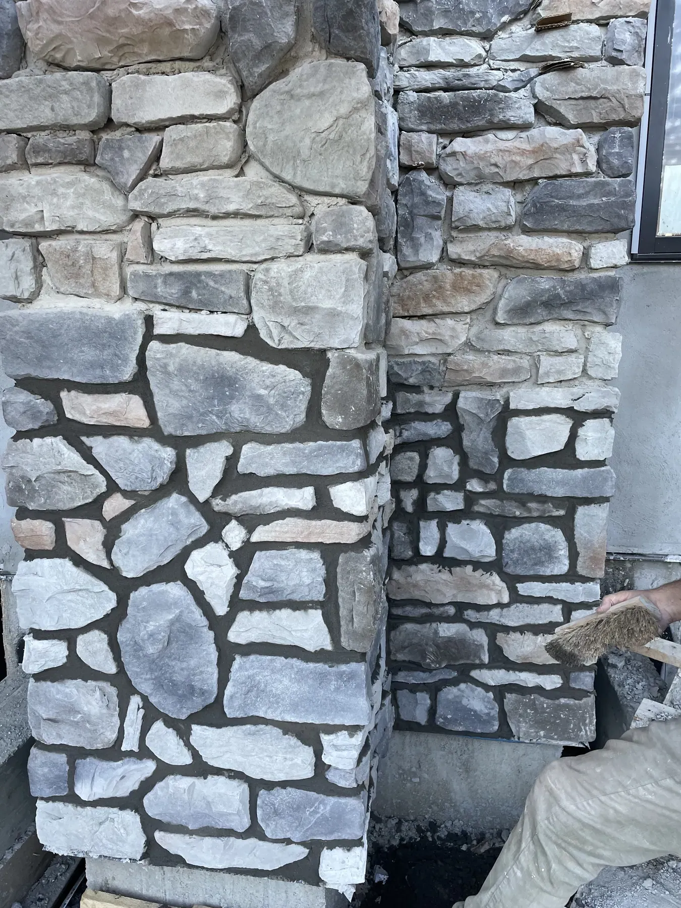 Mason brushing wide mortar joints on a natural stone column during a grouted stone veneer install