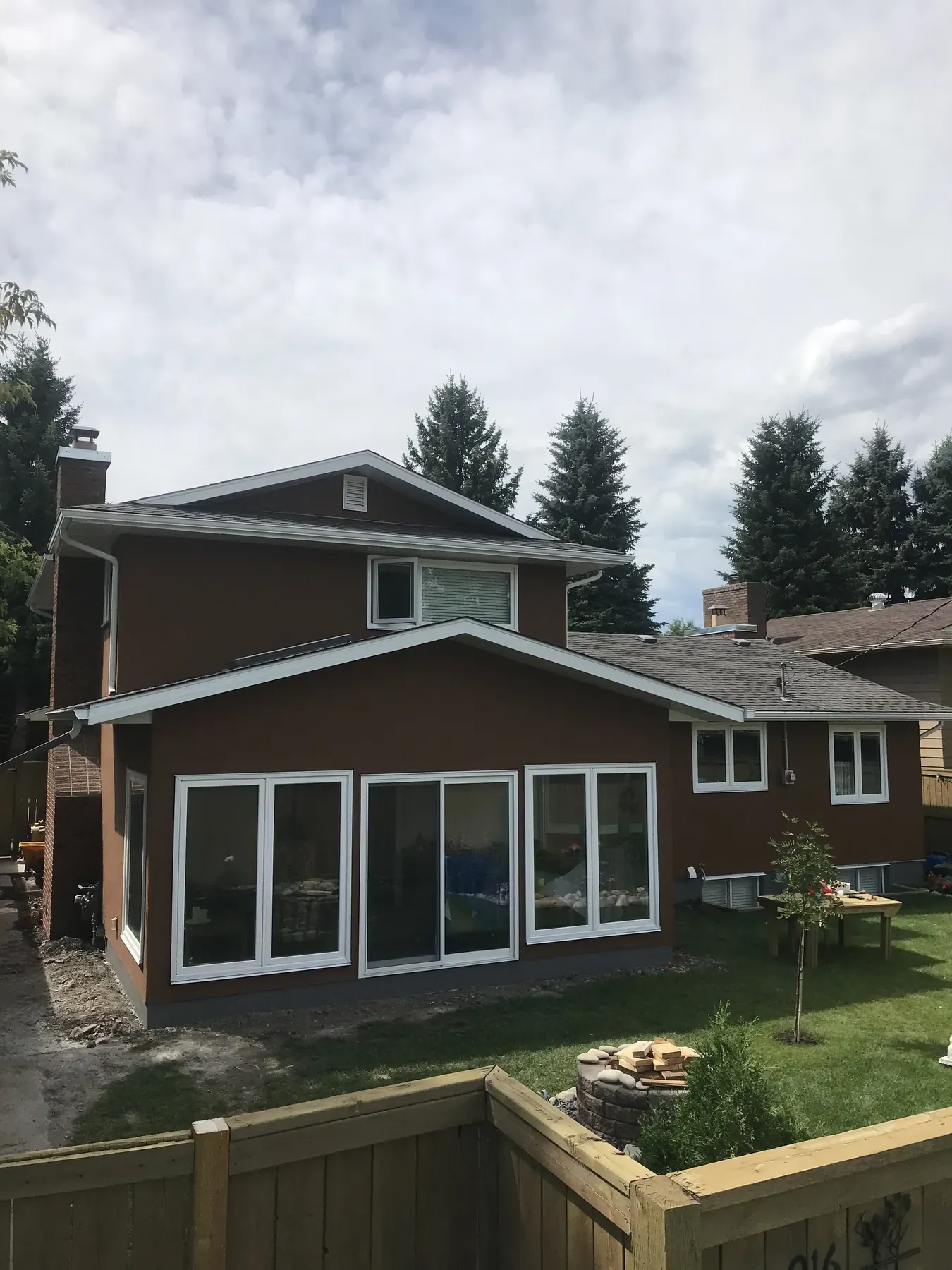 Rear of a two-storey home with brown stucco and new white patio doors and windows after an exterior renovation