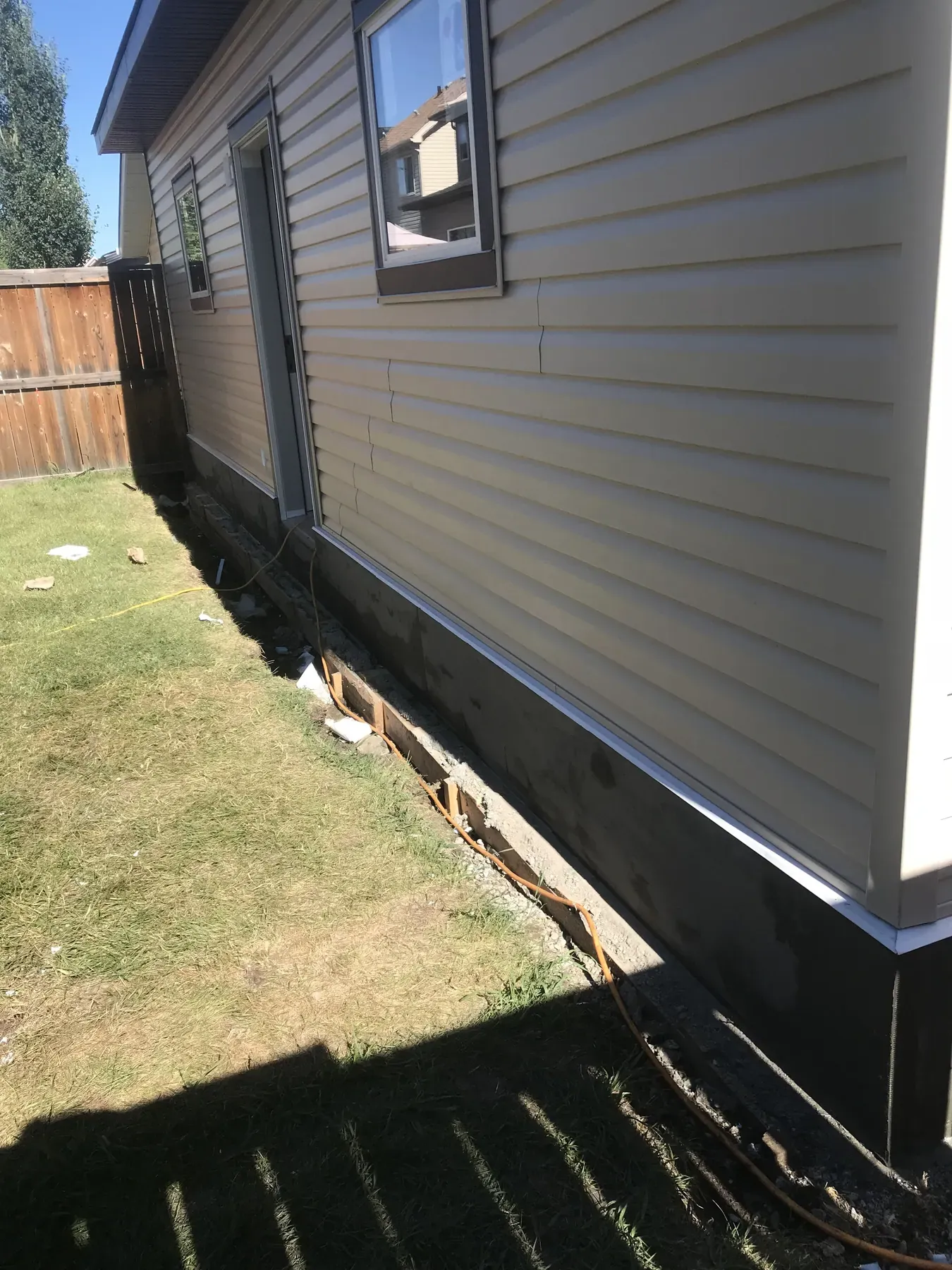 New beige vinyl siding on the side of a house above freshly parged foundation, with the trench still open