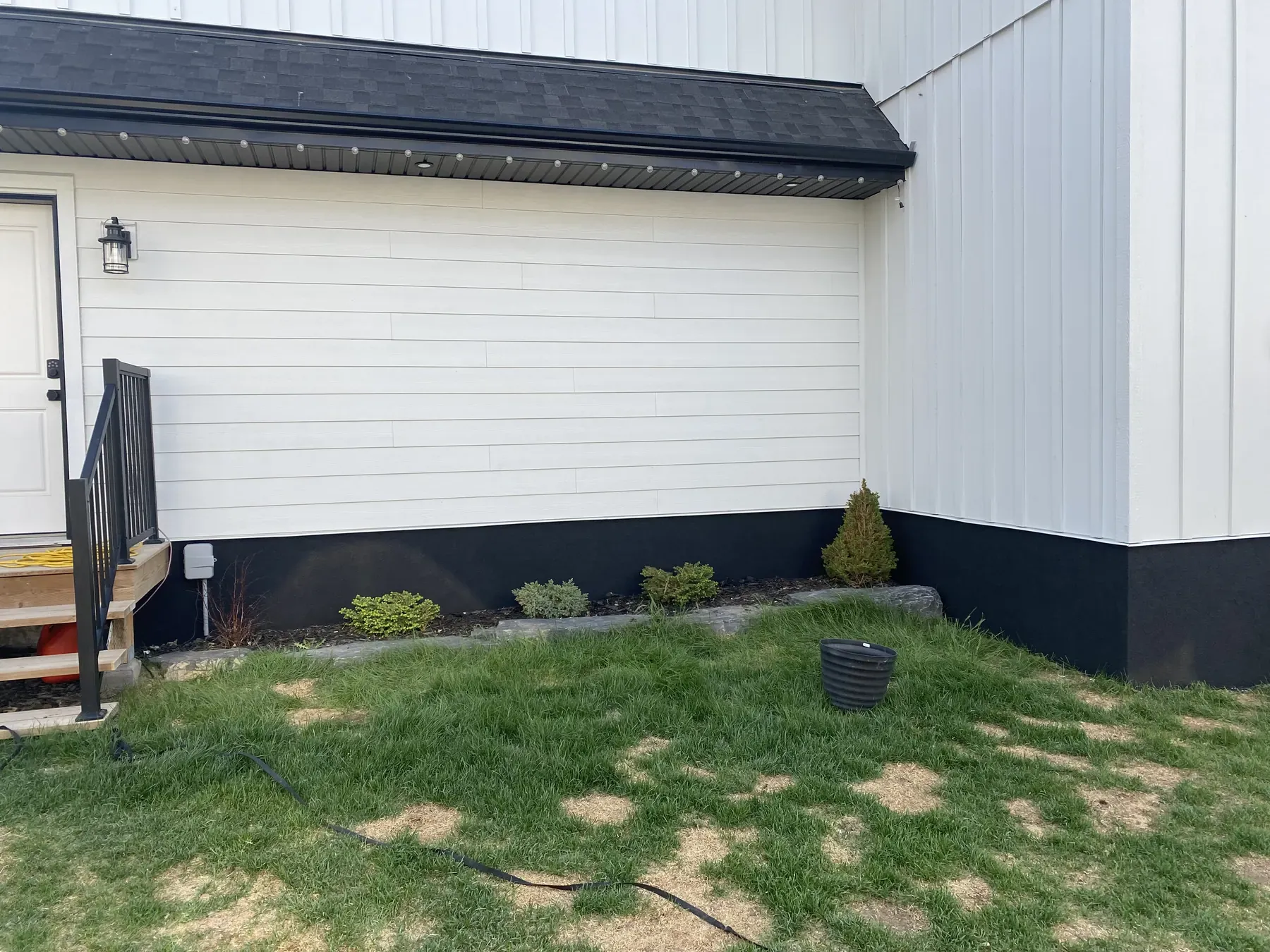 Rear of a home reclad in white lap and vertical siding over a black parged foundation